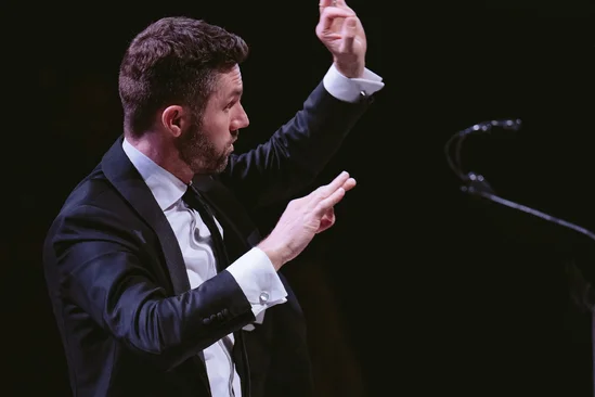 Conductor in a suit leading an orchestra, microphone on the side.